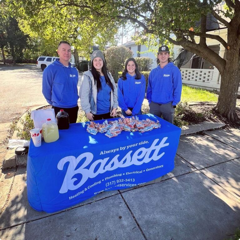 Four Bassett Services team members at a Bassett table during an outdoor community event