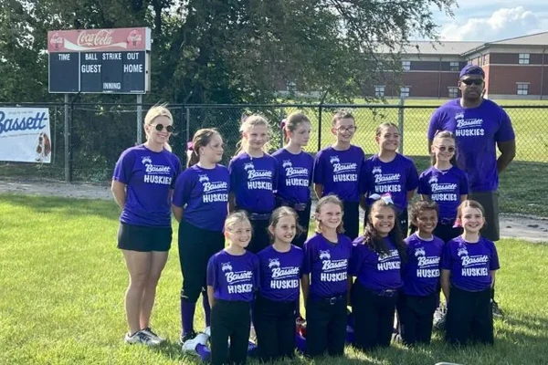 Center Grove Lassie League softball team in purple Bassett-sponsored jerseys posing on the ball field with their coach