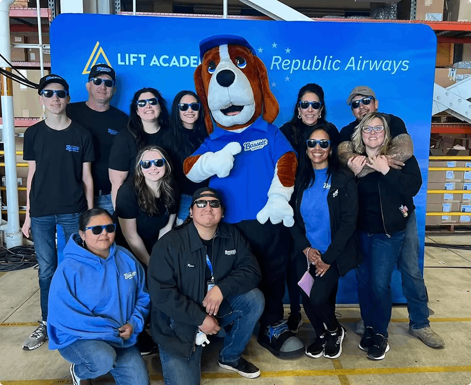 Bassett Services team and hound mascot posing with a group in front of a Lift Academy and Republic Airways backdrop